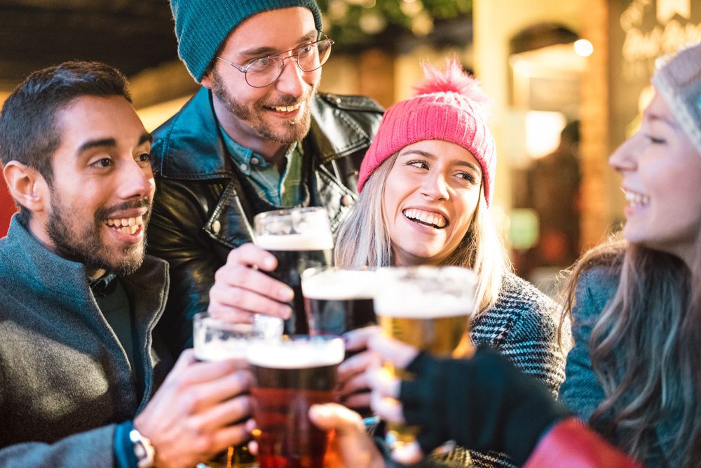 Friends drinking beer at brewery bar outdoor on winter time - Friendship concept with young people having fun together toasting at happy hour promotion - Focus on girl with pink hat - Warm neon filter